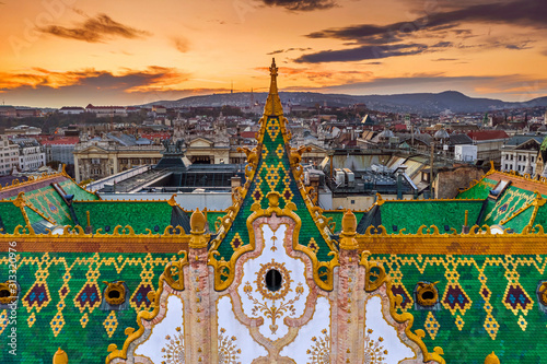 Budapest, Hungary - Aerial view of the famous colorful rooftop of State Treasury building with Fisherman's Bastion and golden sunset at background. Roof tiles has been made from Zsolnay pyrogranite