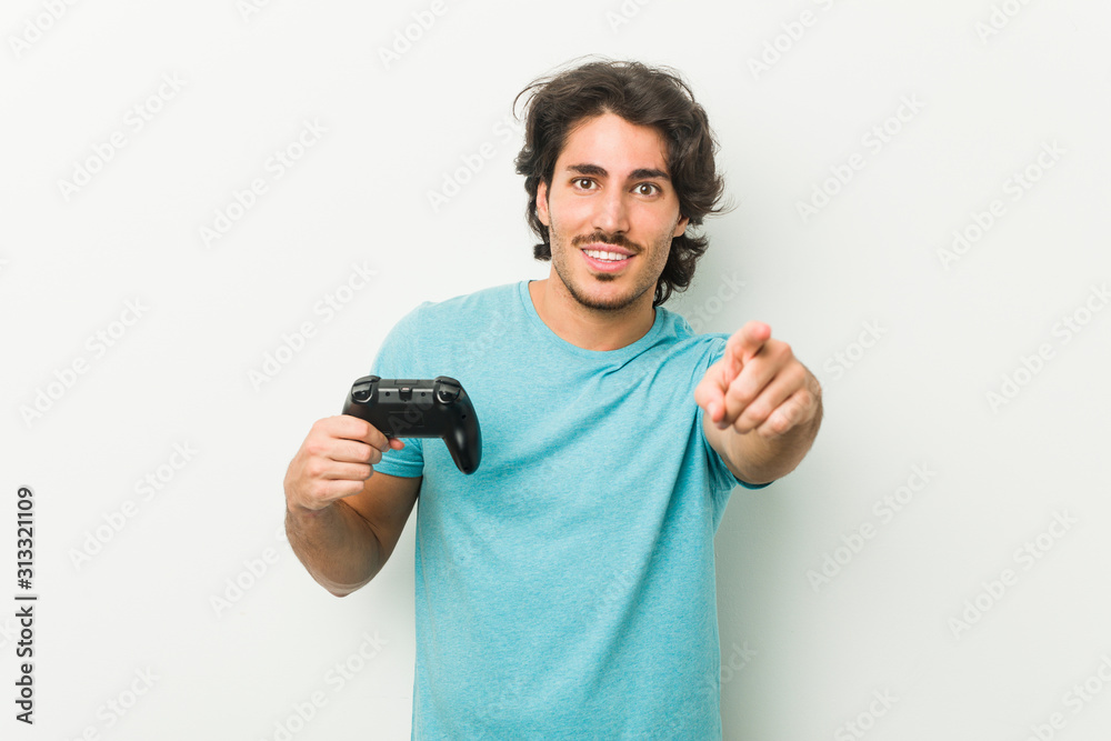 Young man holding a game controller cheerful smiles pointing to front. Young man holding a game controller cheerful smiles pointing to front.