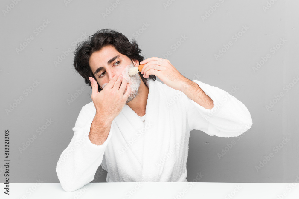 Young caucasian man shaving his beard isolated on a grey background Young caucasian man shaving his beard isolated on a grey background