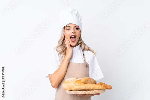 Teenager girl in chef uniform. Female baker holding a table with several breads over isolated white background with surprise facial expression