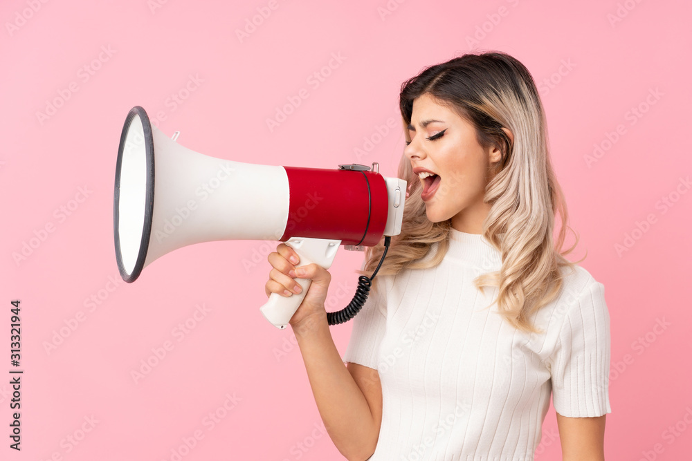 Teenager girl over isolated pink background shouting through a megaphone Teenager girl over isolated pink background shouting through a megaphone