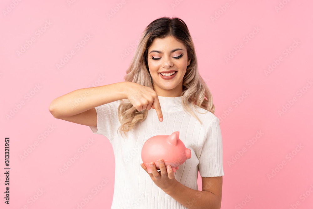 Teenager girl over isolated pink background holding a big piggybank Teenager girl over isolated pink background holding a big piggybank