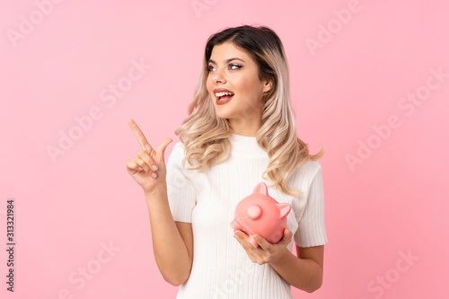 Teenager girl over isolated pink background holding a big piggybank