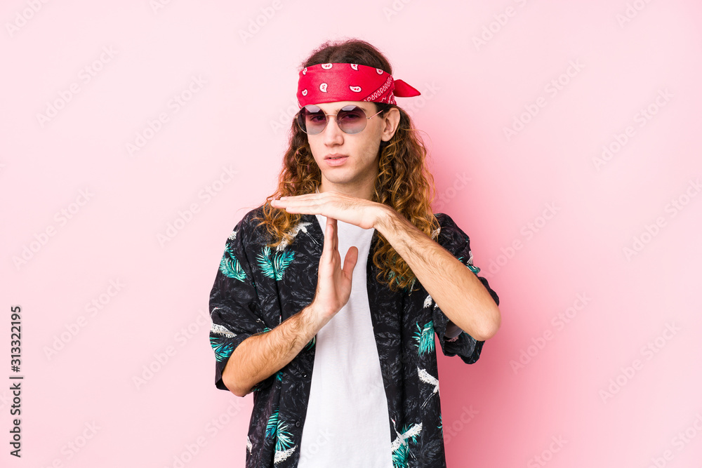Young long hair hippie man posing in a pink background showing a timeout gesture. Young long hair hippie man posing in a pink background showing a timeout gesture.