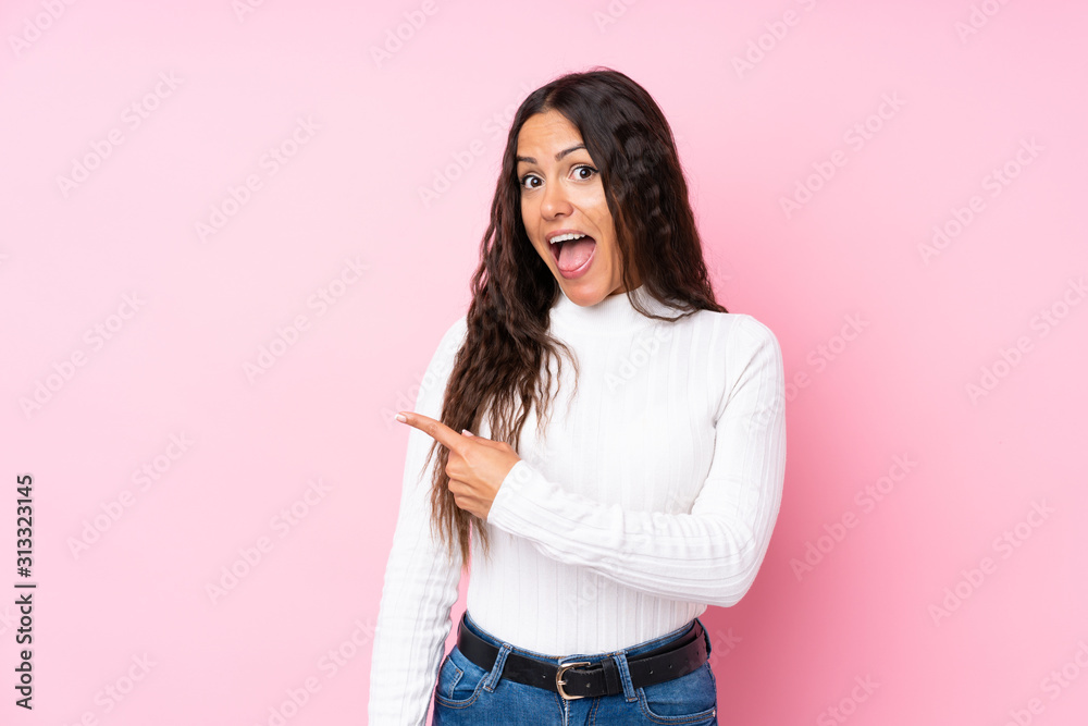 Young woman over isolated pink background surprised and pointing side Young woman over isolated pink background surprised and pointing side
