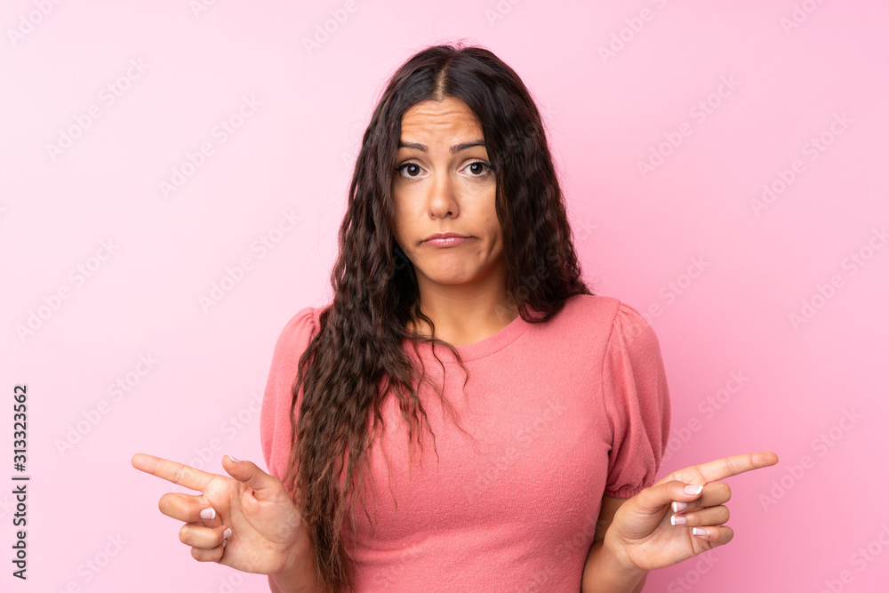 Young woman over isolated pink background pointing to the laterals having doubts Young woman over isolated pink background pointing to the laterals having doubts