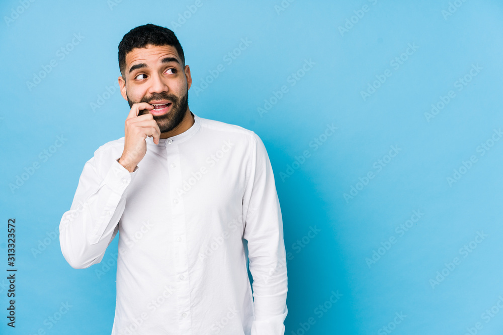 Young latin man against a blue  background isolated relaxed thinking about something looking at a copy space.