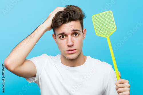 Young caucasian man holding a fly swatter being shocked, she has remembered important meeting.