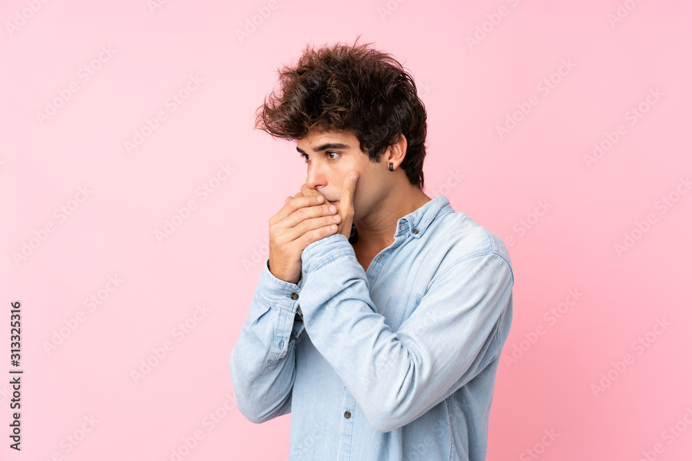 Young caucasian man with jean shirt over isolated pink background covering mouth and looking to the side Young caucasian man with jean shirt over isolated pink background covering mouth and looking to the side