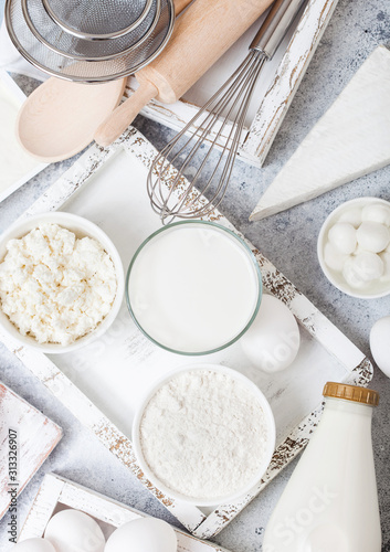 Fresh dairy products on white table background. Glass of milk, bowl of flour and cottage cheese and eggs. Box of baking utensils. whisk and spatula in vintage wooden box.Top view.