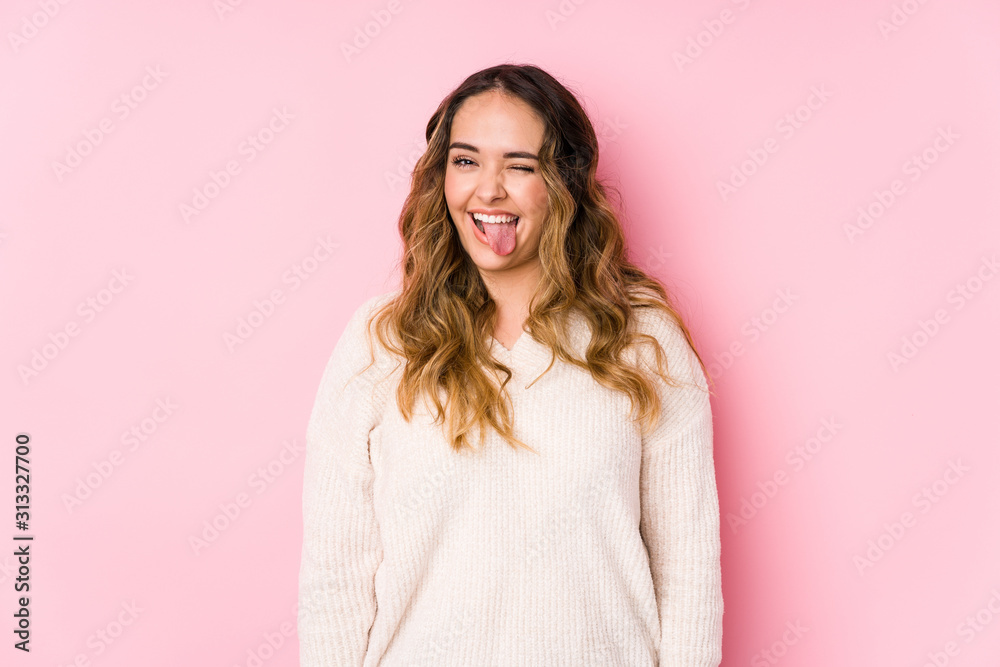 Young curvy woman posing in a pink background isolated funny and friendly sticking out tongue.