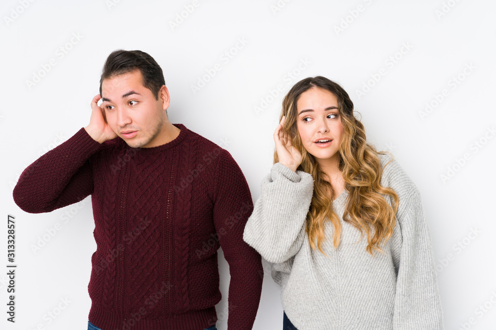 Young couple posing in a white background trying to listening a gossip. Young couple posing in a white background trying to listening a gossip.