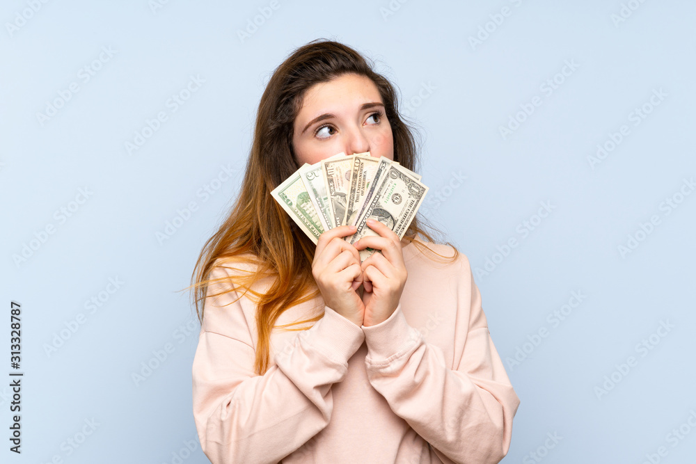 Young brunette girl over isolated blue background taking a lot of money Young brunette girl over isolated blue background taking a lot of money