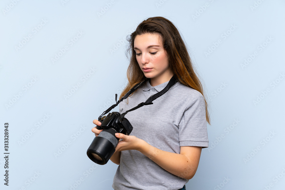 Young brunette girl over isolated blue background with a professional camera Young brunette girl over isolated blue background with a professional camera