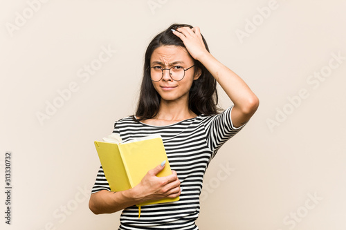 Young asian woman student holding a book being shocked, she has remembered important meeting.
