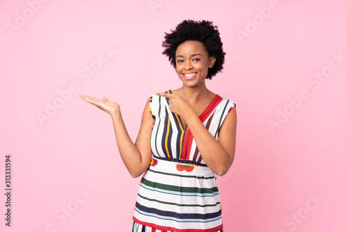 African american woman over isolated pink background holding copyspace imaginary on the palm to insert an ad