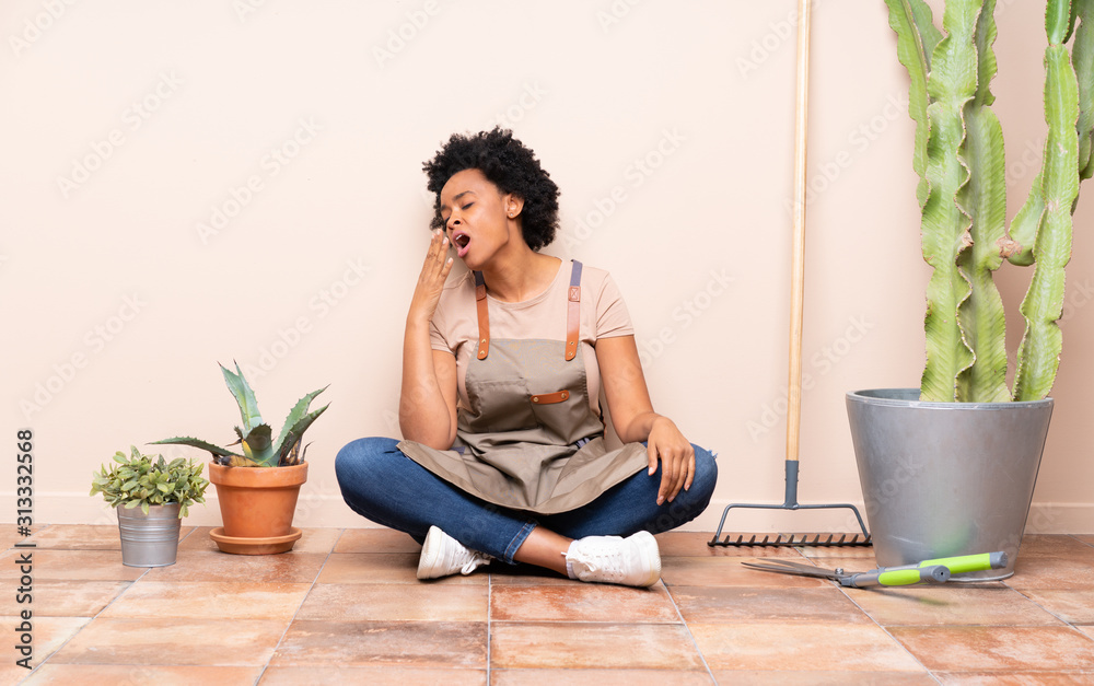 Gardener woman sitting on the floor yawning and covering wide open mouth with hand Gardener woman sitting on the floor yawning and covering wide open mouth with hand