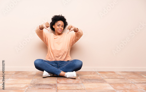 African american woman sitting on the floor showing thumb down © luismolinero