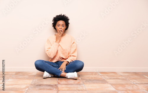 African american woman sitting on the floor surprised and shocked while looking right