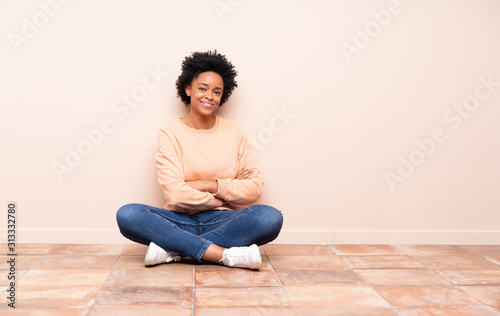 African american woman sitting on the floor with arms crossed and looking forward © luismolinero