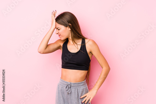 Young caucasian fitness woman posing in a pink background forgetting something  slapping forehead with palm and closing eyes.