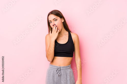 Young caucasian fitness woman posing in a pink background yawning showing a tired gesture covering mouth with hand.