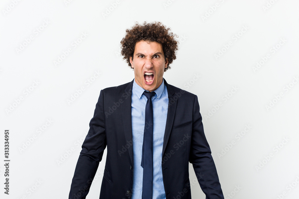 Young business curly man against white background screaming very angry and aggressive. Young business curly man against white background screaming very angry and aggressive.