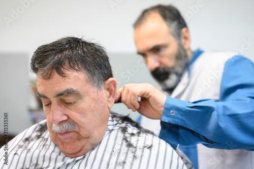 Barber trimming hair of old man at barber shop .