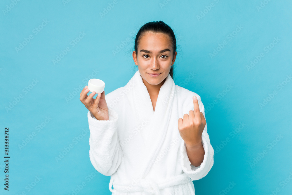 Young mixed race indian holding a moisturizer pointing with finger at you as if inviting come closer. Young mixed race indian holding a moisturizer pointing with finger at you as if inviting come closer.