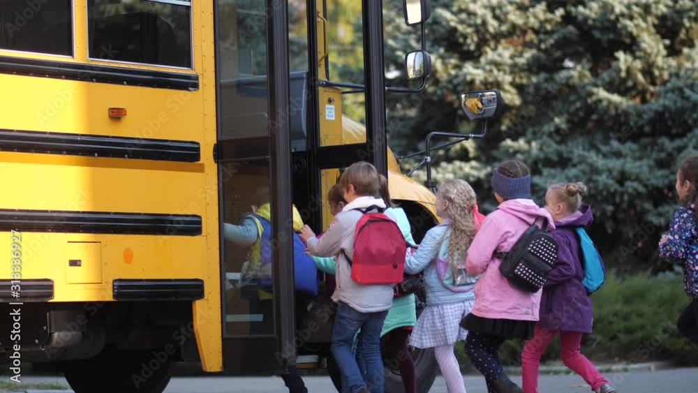 Cute schoolkids running in crowd to school bus standing with open doors near school. Happy elementary age children rushing home after lessons and pushing while getting on school bus waiting for them
