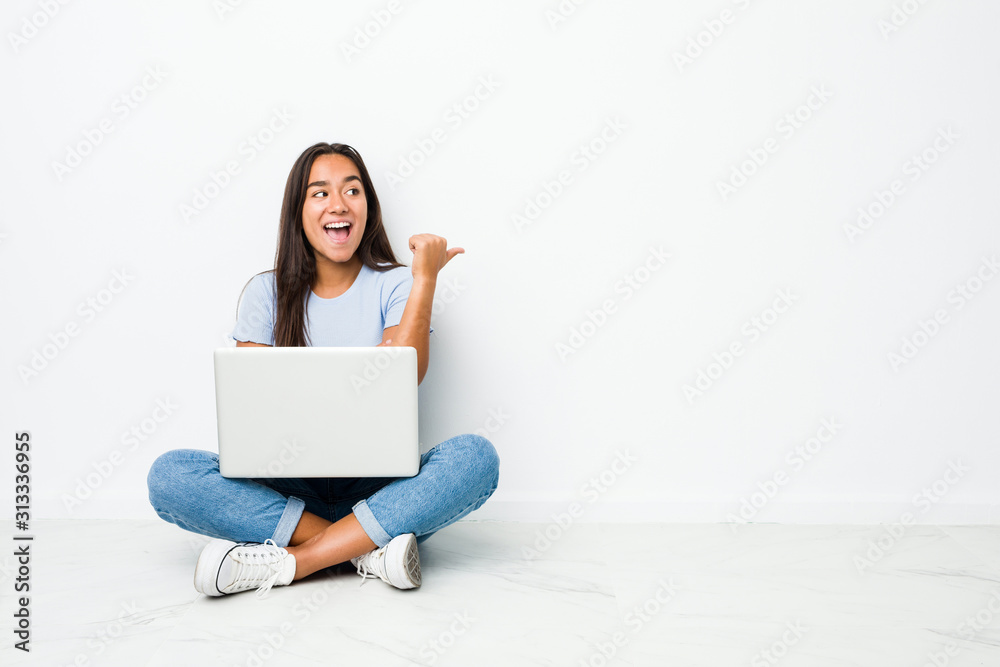 Young mixed race indian woman sitting working on laptop points with thumb finger away, laughing and carefree. Young mixed race indian woman sitting working on laptop points with thumb finger away, laughing and carefree.