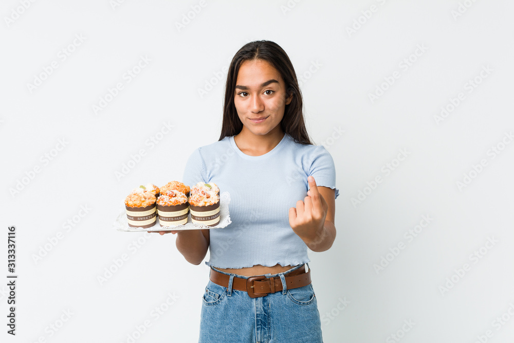 Young mixed race indian holding a sweet cakes pointing with finger at you as if inviting come closer. Young mixed race indian holding a sweet cakes pointing with finger at you as if inviting come closer.