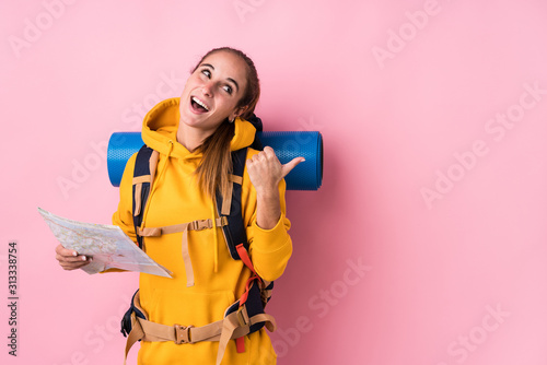 Young traveler caucasian woman isolated points with thumb finger away, laughing and carefree. © Asier