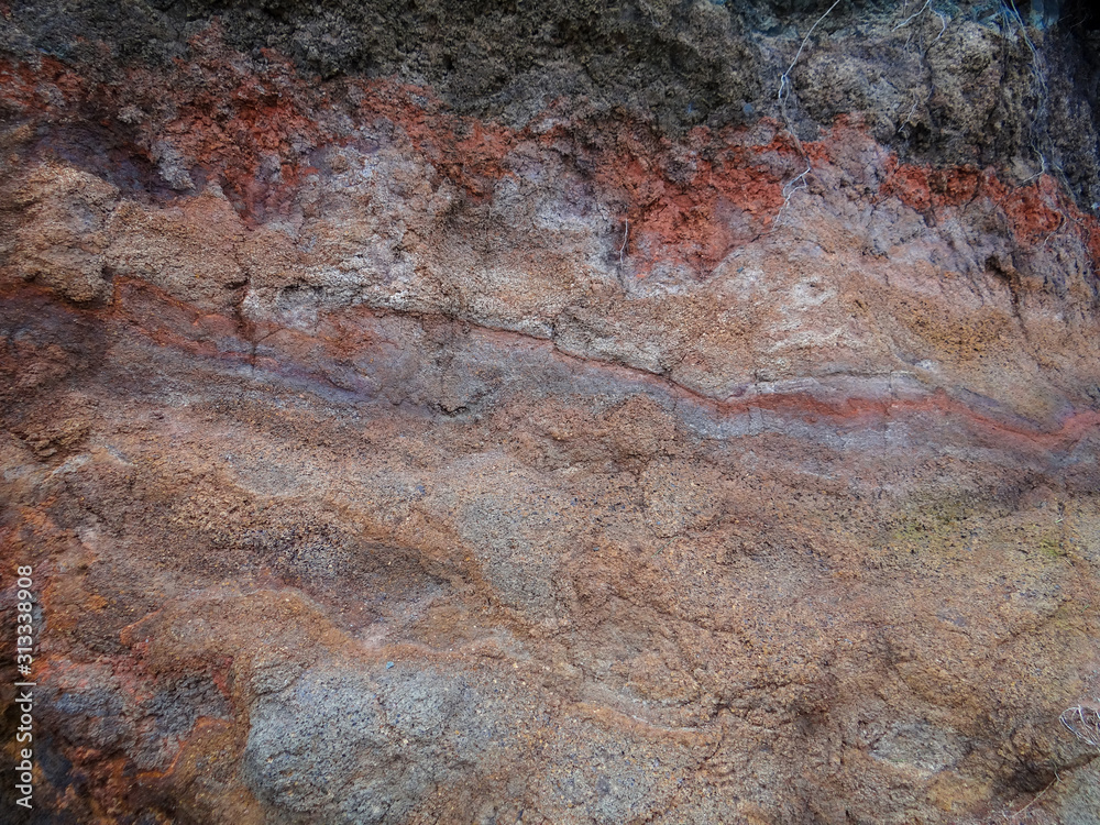 Obraz premium Mottled color of purples and grays and reds show in this picture of a dirt cliff alongside a road in Maui.