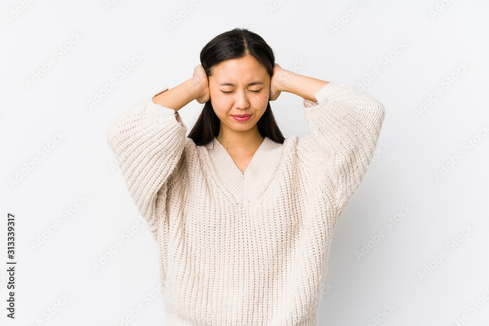 Young chinese woman isolated covering ears with hands trying not to hear too loud sound.