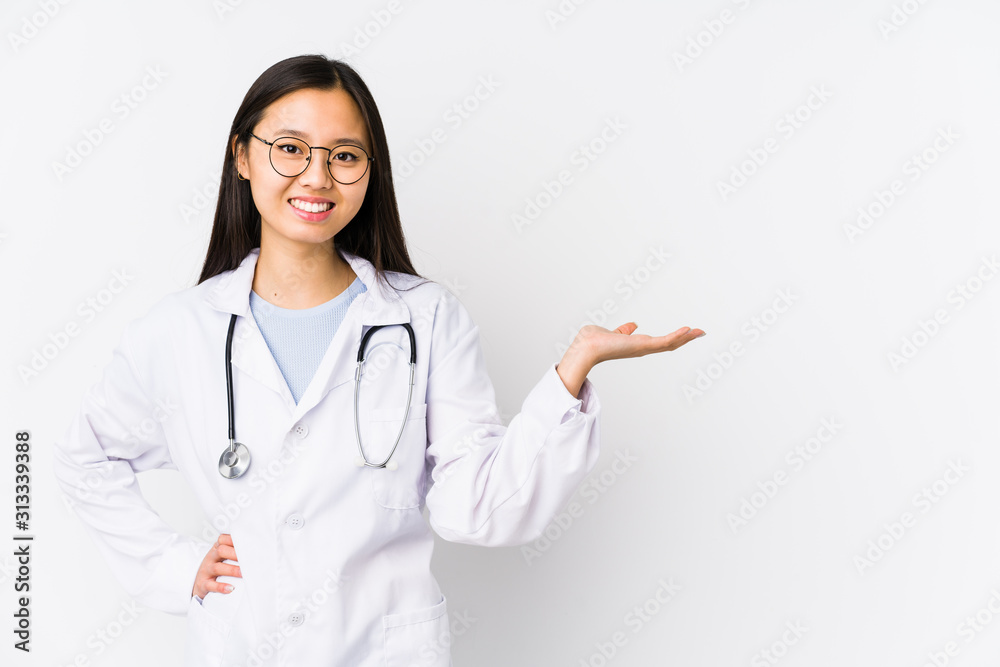 Young doctor chinese woman isolated showing a copy space on a palm and holding another hand on waist. Young doctor chinese woman isolated showing a copy space on a palm and holding another hand on waist.