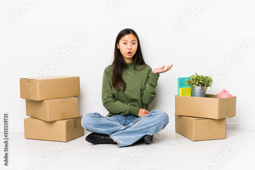 Young chinese woman moving to a new home impressed holding copy space on palm.