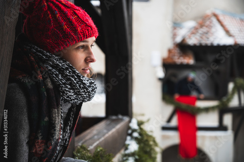 Beautiful young woman looking at the landscape from a balcony with winter clothes, hat, scarf and coat