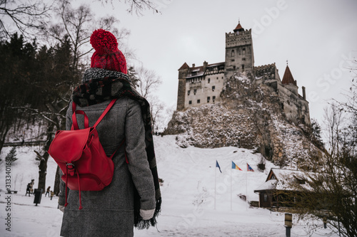 Fototapeta Naklejka Na Ścianę i Meble -  Beautiful young woman watching a medieval castle and dressed in winter clothes. Bran Castle, better known as Dracula's Castle
