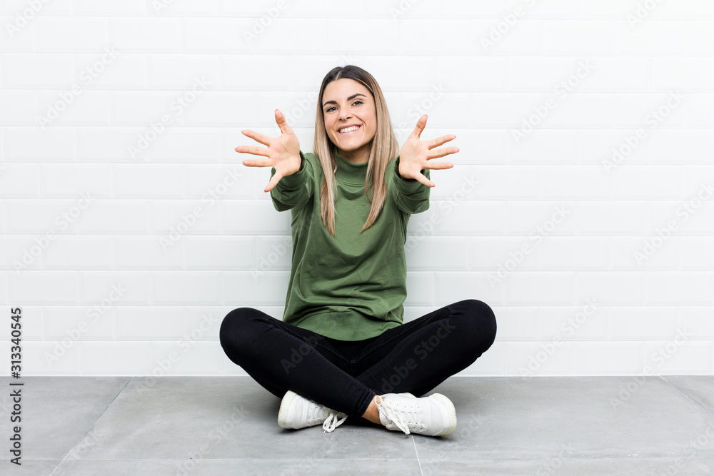 Young caucasian woman sitting on the floor feels confident giving a hug to the camera. Young caucasian woman sitting on the floor feels confident giving a hug to the camera.