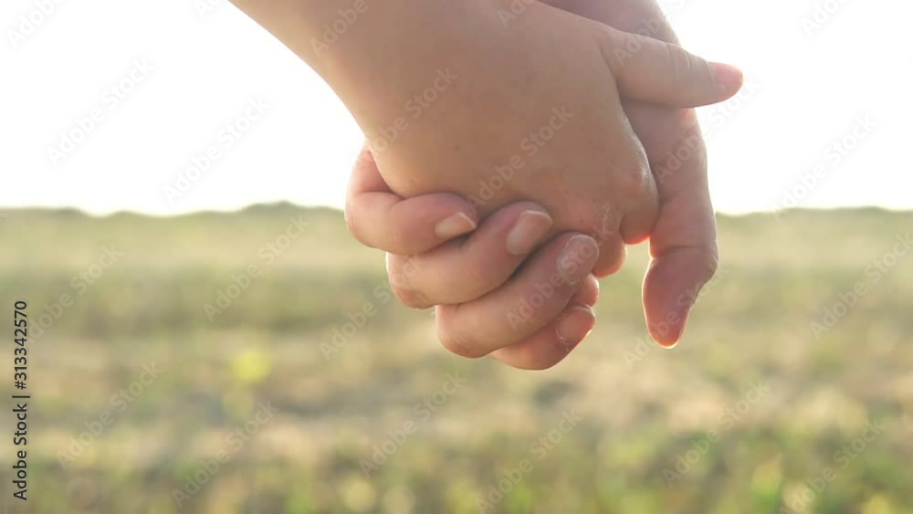 Couple holding hands and walking away through the green field. Man takes woman's hand then holds it and they start to go away while the sun shines brightly.