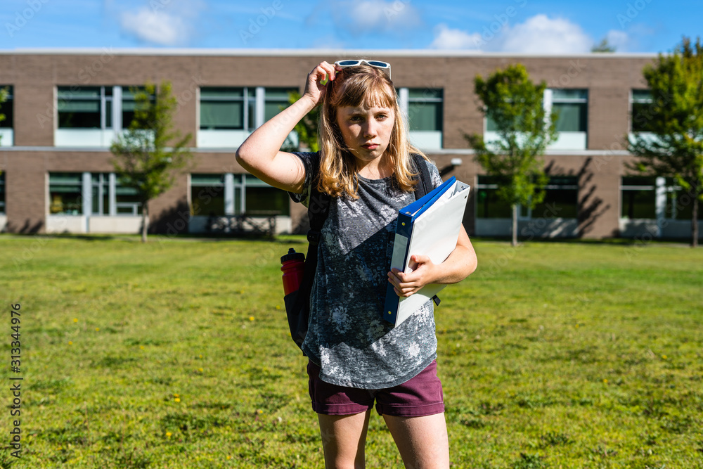 Depressed/Sad Student standing in front of High School while holding binders. Depressed/Sad Student standing in front of High School while holding binders.
