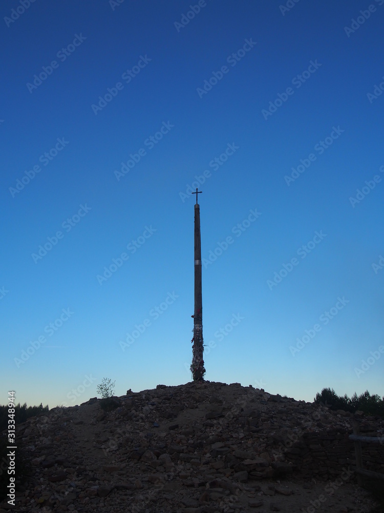 Fototapeta premium Beautiful blue sky with Cruz de Ferro (Cross of Iron) in the early morning on the road to Santiago de Compostela, Camino de Santiago, Way of St. James, Foncebadon to Ponferrada, French way, Spain