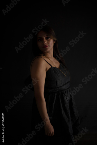 Fashion portrait of an young and attractive Indian Bengali brunette girl with black western dress in front of a black studio background. Indian fashion portrait and lifestyle.
