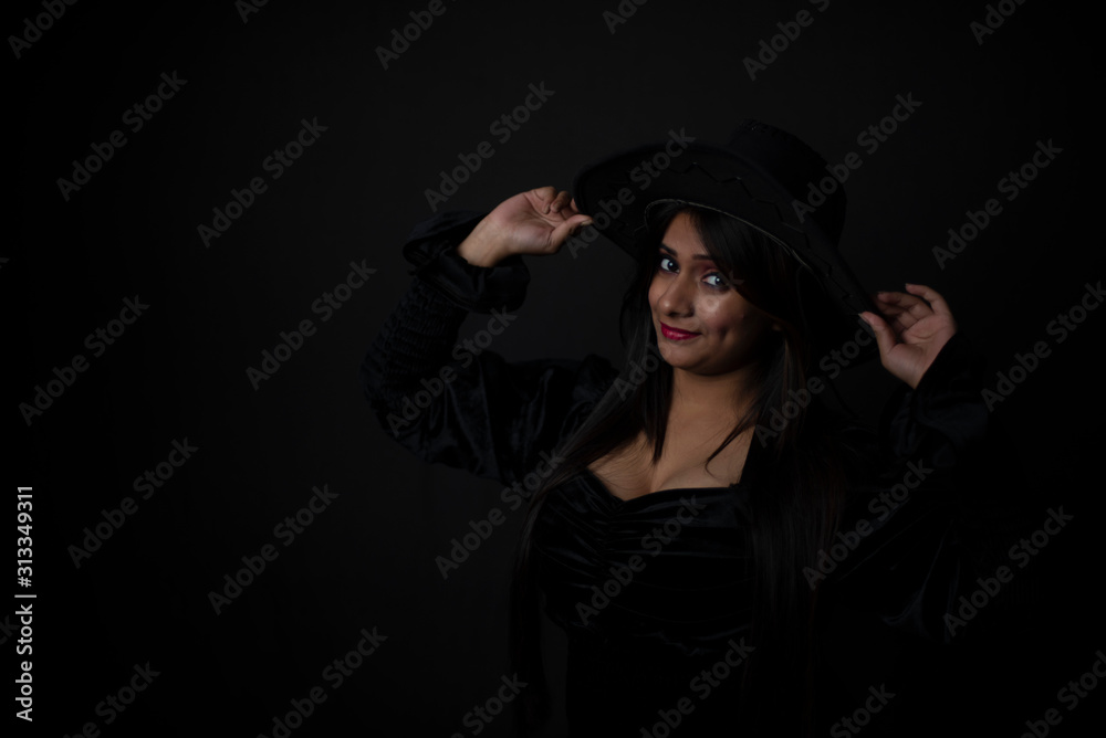 Fashion portrait of an young and attractive Indian Bengali brunette girl with black western dress with a cowboy hat in front of a black studio background. Indian fashion portrait and lifestyle. Fashion portrait of an young and attractive Indian Bengali brunette girl with black western dress with a cowboy hat in front of a black studio background. Indian fashion portrait and lifestyle.