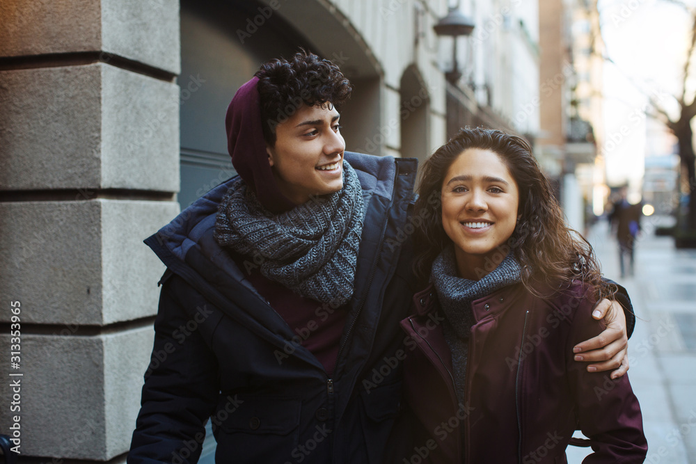 Portrait of a happy young hispanic couple smiling and holding each other while walking outside in the city on a sunny day