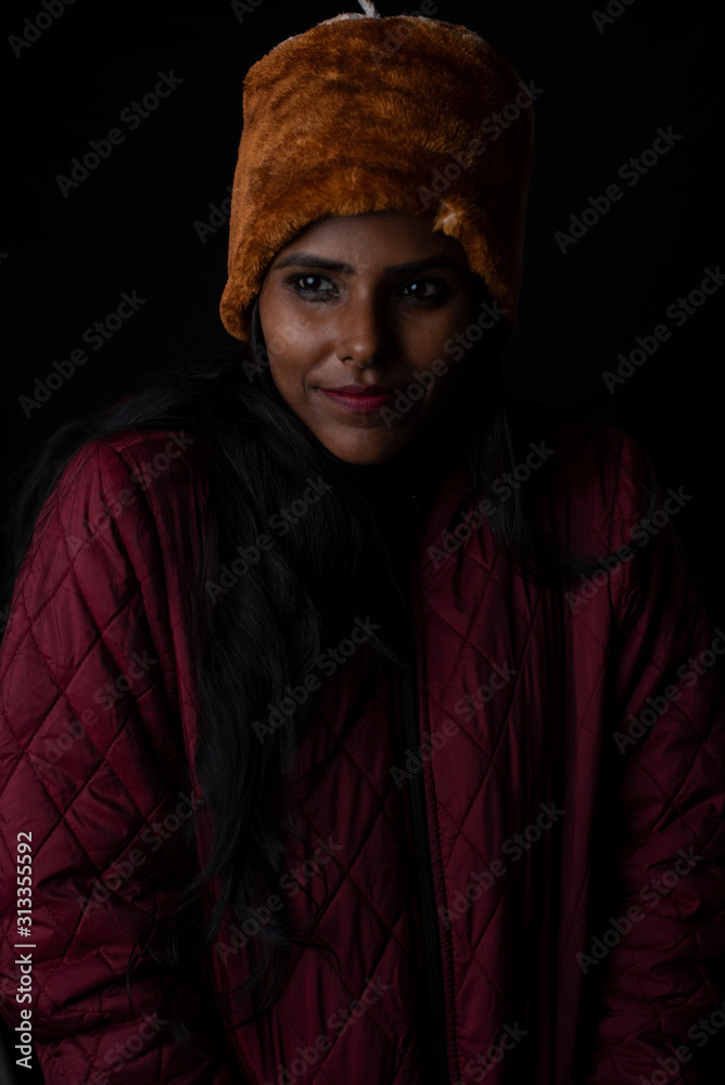 Portrait of an young and attractive dark skinned Indian woman wearing woolen cap and jacket feeling cold in a winter night in dark background. Winter and Christmas Portrait of an young and attractive dark skinned Indian woman wearing woolen cap and jacket feeling cold in a winter night in dark background. Winter and Christmas