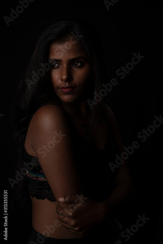 Fashion portrait of an Indian brunette Bengali dark skinned woman with black lingerie standing in black studio copy space background. Indian fashion photography and lifestyle.