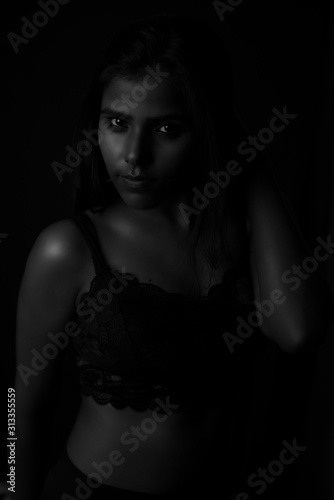 Monochrome fashion portrait of an Indian brunette Bengali dark skinned woman with black lingerie standing in black studio copy space background. Indian fashion photography and lifestyle.