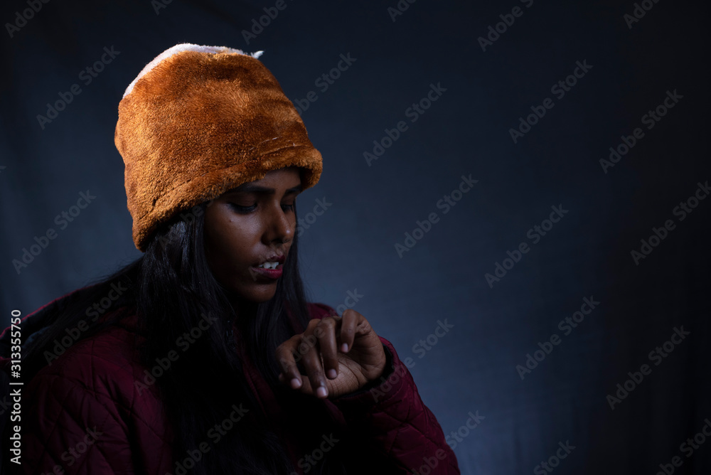 Portrait of an young and attractive dark skinned Indian woman wearing woolen cap and jacket feeling cold in a winter night in dark background. Winter and Christmas Portrait of an young and attractive dark skinned Indian woman wearing woolen cap and jacket feeling cold in a winter night in dark background. Winter and Christmas